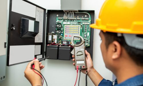 Electrician working use digital clamp meter in hands of electrician, close-up against background of electrical wires and relays. Adjustment of scheme of automation and control of electrical equipment