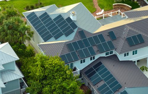 New american residential house with rooftop covered with solar photovoltaic panels for producing of clean electrical energy in suburban rural area. Concept of investment in autonomous home.